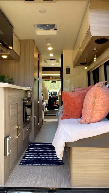 Cozy RV rental interior with light wood cabinetry, a comfortable bed, compact kitchen area, and view to the front cabin.