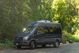 Explore nature with this dark blue Mercedes Sprinter camper van. An ideal RV rental, parked in a vibrant forest setting.