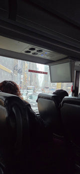 Inside a bus: a rain-streaked view of a bustling city street with traffic. Plan your next adventure, maybe an RV rental trip!