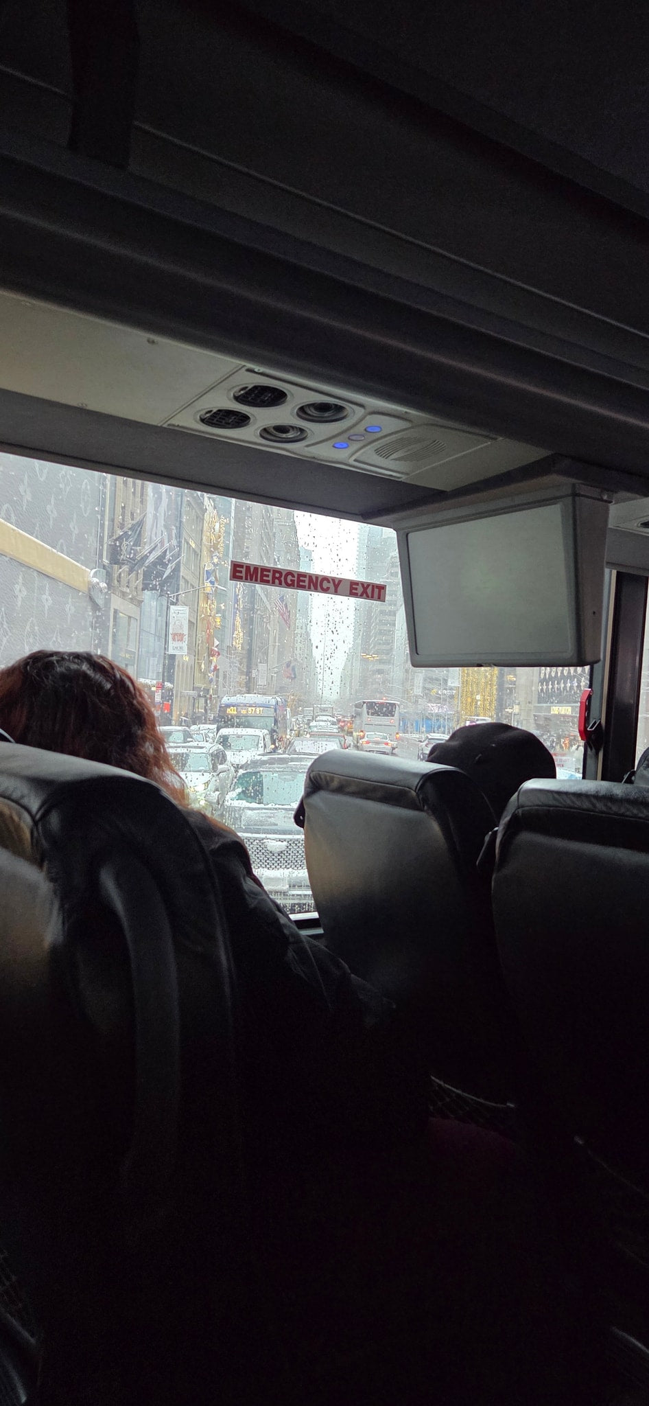 Inside a bus: a rain-streaked view of a bustling city street with traffic. Plan your next adventure, maybe an RV rental trip!