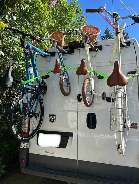 RV rental van with 3 bikes mounted vertically on a rear rack: a blue adult bike, two smaller ones with baskets. Ready for trails!
