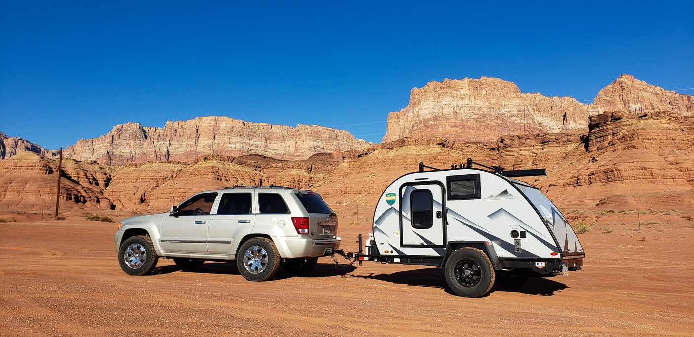 SUV towing a teardrop RV rental in a stunning desert landscape with red rock mountains. Perfect for an outdoor adventure!