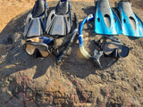 Two sets of snorkeling fins, masks, and snorkels rest on a rock, ideal gear for an RV rental beach getaway.