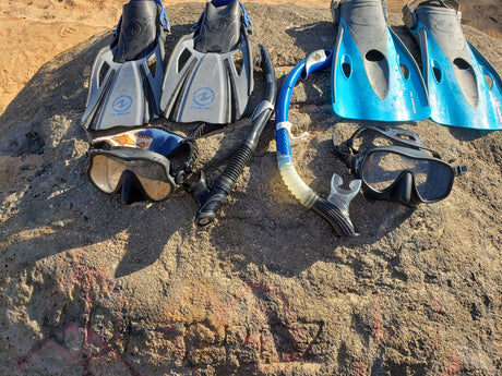 Two sets of snorkeling fins, masks, and snorkels rest on a rock, ideal gear for an RV rental beach getaway.