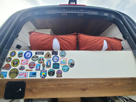 Cozy RV rental bed with pillows & a wall of travel patches showcasing US state parks & landmarks visited.