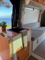 Serene RV rental interior: modern kitchen with sink & plant, offering an amazing ocean view. Perfect for van life adventures!