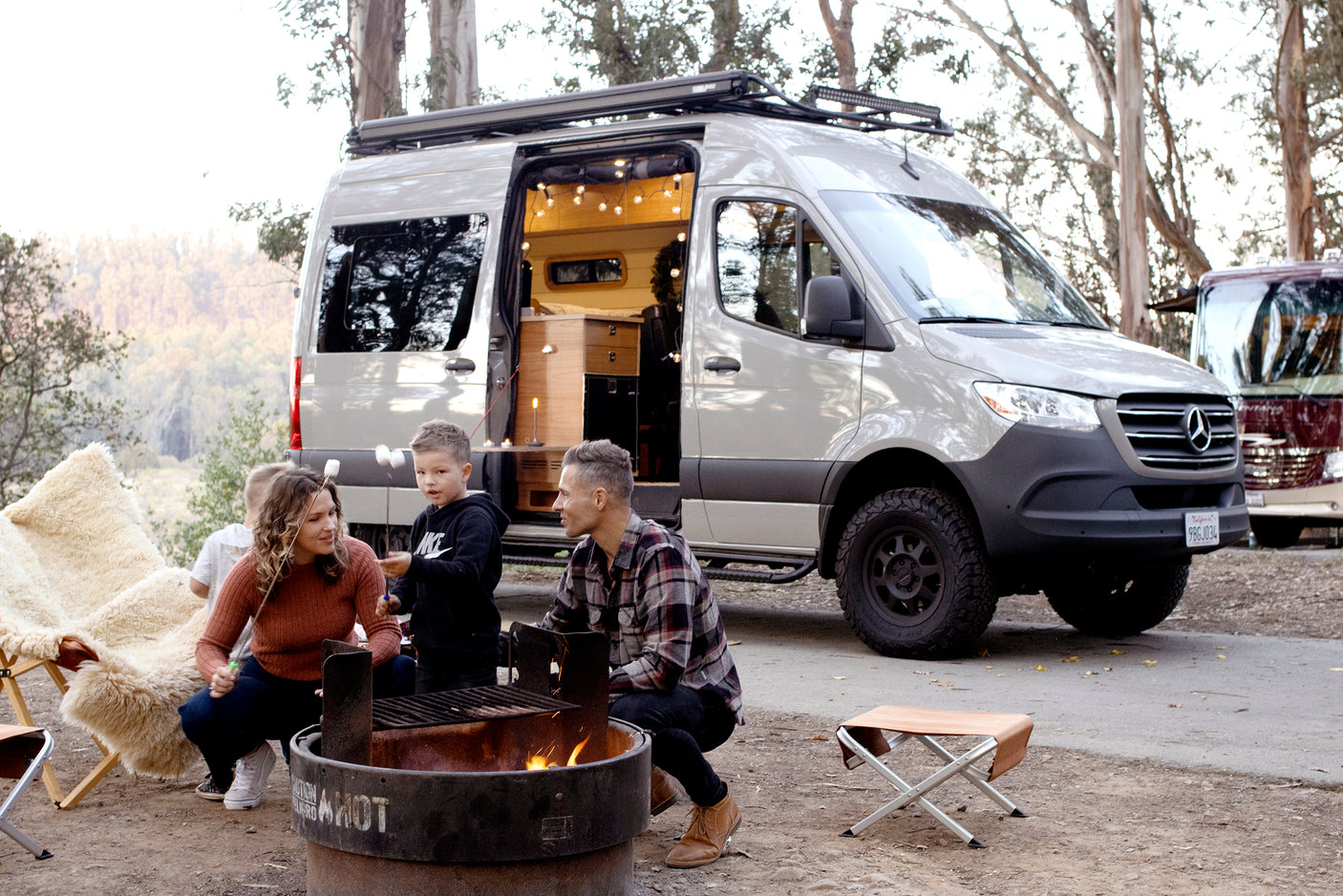 Family enjoying an RV rental adventure, roasting marshmallows around the fire pit with their cozy camper van nearby.