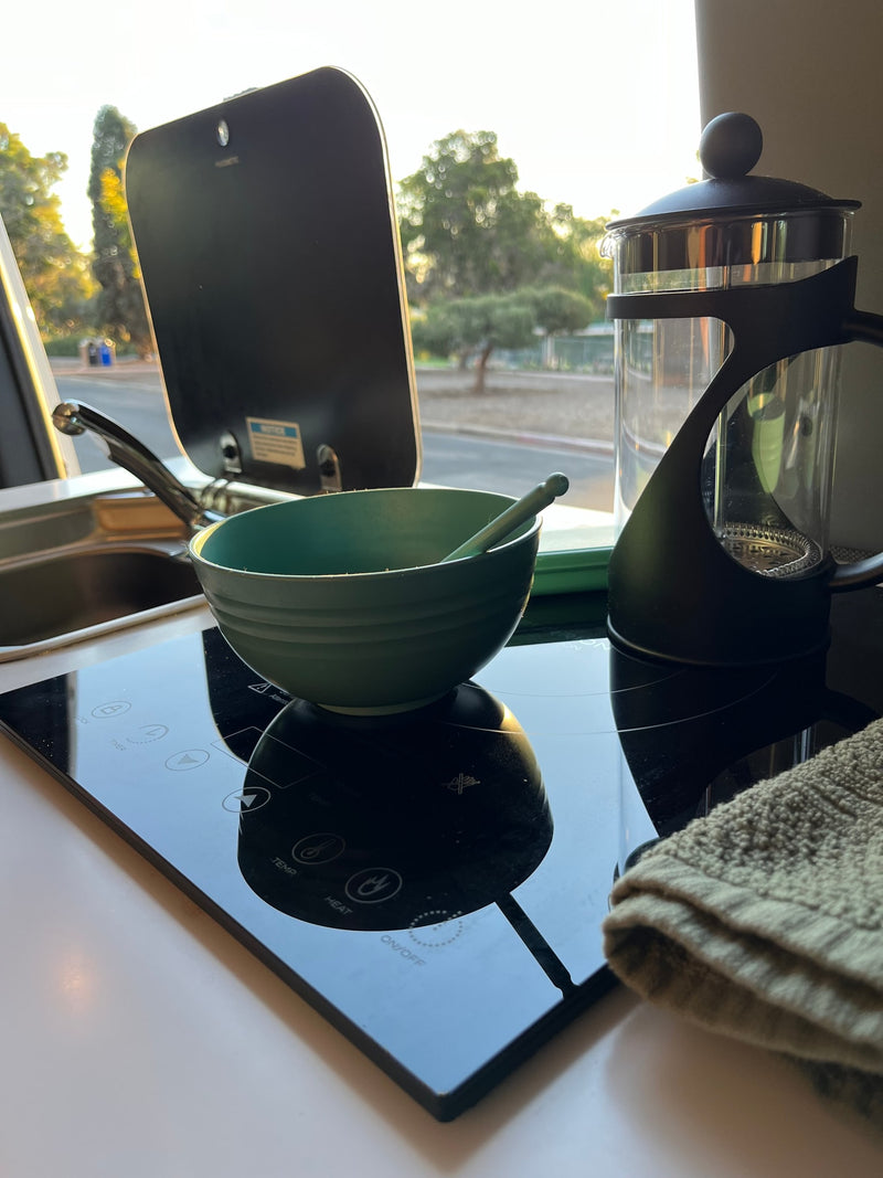 RV rental kitchen setup, featuring an induction cooktop, French press, and a bowl with a spoon, bathed in morning light. — photo 5