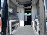 Interior of an RV rental camper van, showing the rear multi-functional living space with benches, storage, and view to the cab.