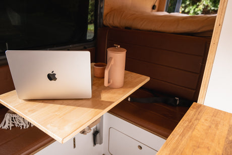 RV rental workspace: MacBook, coffee, and cozy seating inside a modern camper van for remote work and travel.