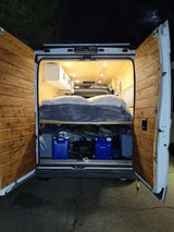 Inside this **rv rental** camper van: a wood-paneled interior with a bed, under-bed storage, and bright lights. Perfect for off-grid travel.