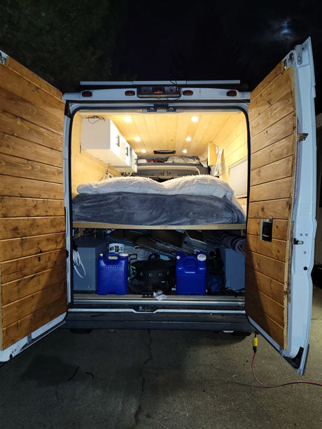 Inside this **rv rental** camper van: a wood-paneled interior with a bed, under-bed storage, and bright lights. Perfect for off-grid travel.