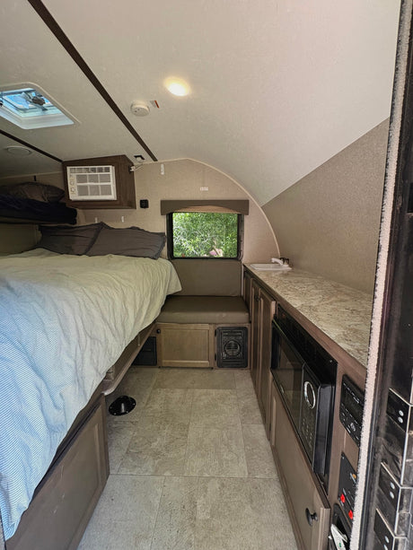 RV rental interior featuring a cozy bed, compact kitchenette, window view, and functional design elements throughout.