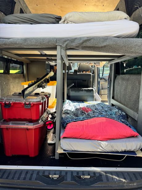 Inside this RV rental: a practical camper van interior with bunk beds, smart storage for gear like skis, and a portable fridge.