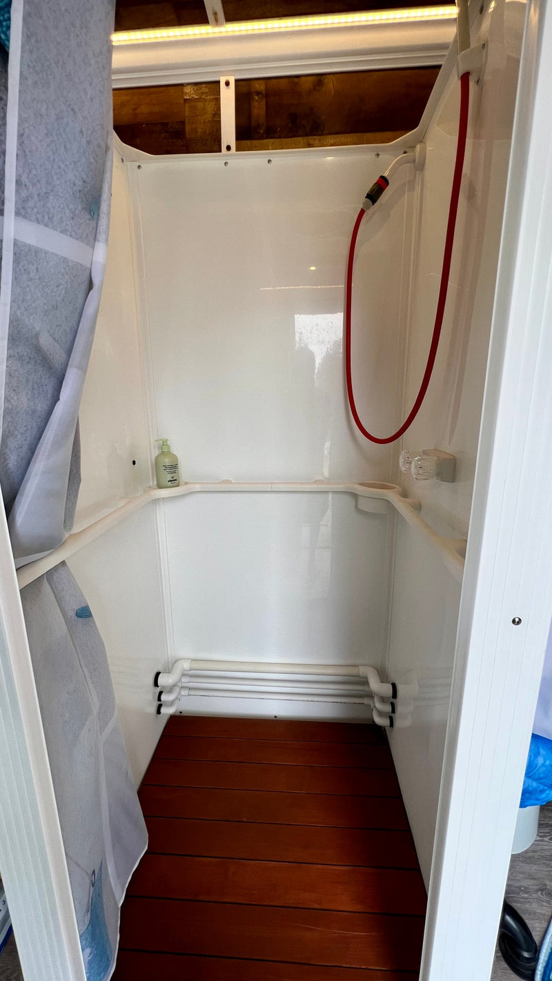 Compact white shower enclosure with red hose shower, wood floor, soap, in an rv rental. — photo 12