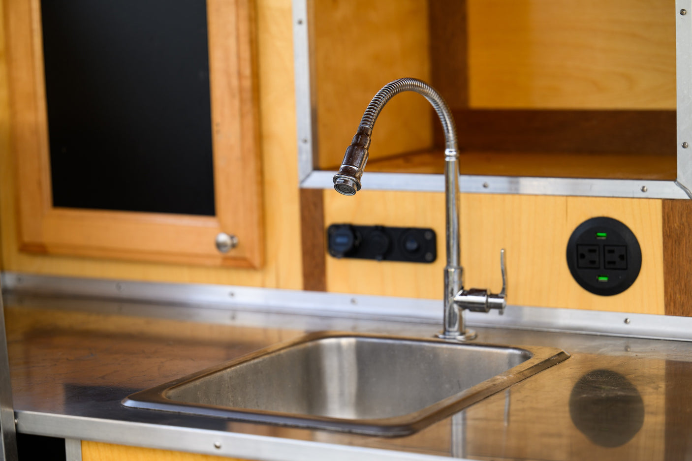 Compact RV rental kitchen with stainless sink, flexible faucet, wood cabinets, and power outlets. Ideal for travel.