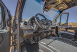 Interior view of an RV rental van's driver cockpit, featuring a modern dashboard and open door to scenic mountains.