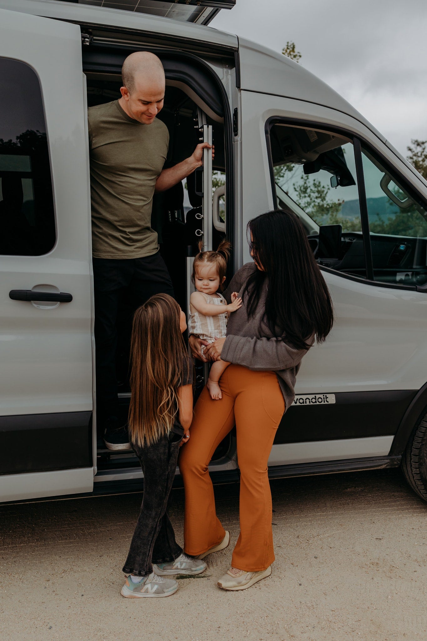 Family by their rv rental camper van. Dad in door, mom holds baby, older child watches. Fun family travel. — photo 20