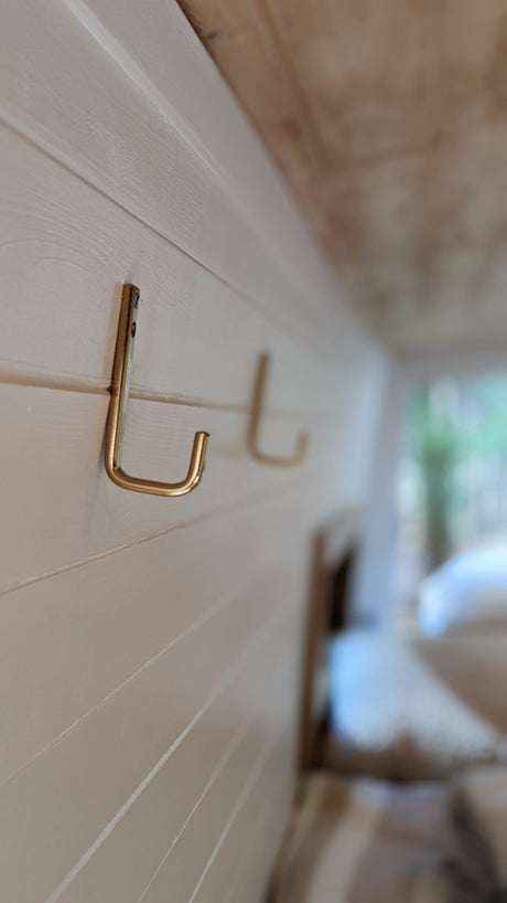 Stay organized on your RV rental journey! Close-up of gold hooks on the cozy, paneled interior wall of an RV.