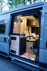 Explore this modern RV rental's inviting interior. Open side door reveals cozy seating, kitchenette, and colorful rug.