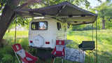 **RV rental** setup with an extended awning, chairs, and tables, perfect for outdoor camping in a grassy field.