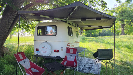 **RV rental** setup with an extended awning, chairs, and tables, perfect for outdoor camping in a grassy field.