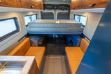 Explore this RV rental's spacious camper van interior featuring an elevated bed, comfy benches, and a convenient kitchen.