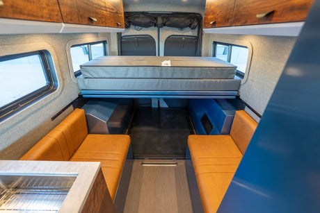 Explore this RV rental's spacious camper van interior featuring an elevated bed, comfy benches, and a convenient kitchen.