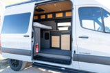 Open side door of an rv rental camper van reveals a custom interior with bed, kitchen, storage, and fire extinguisher.