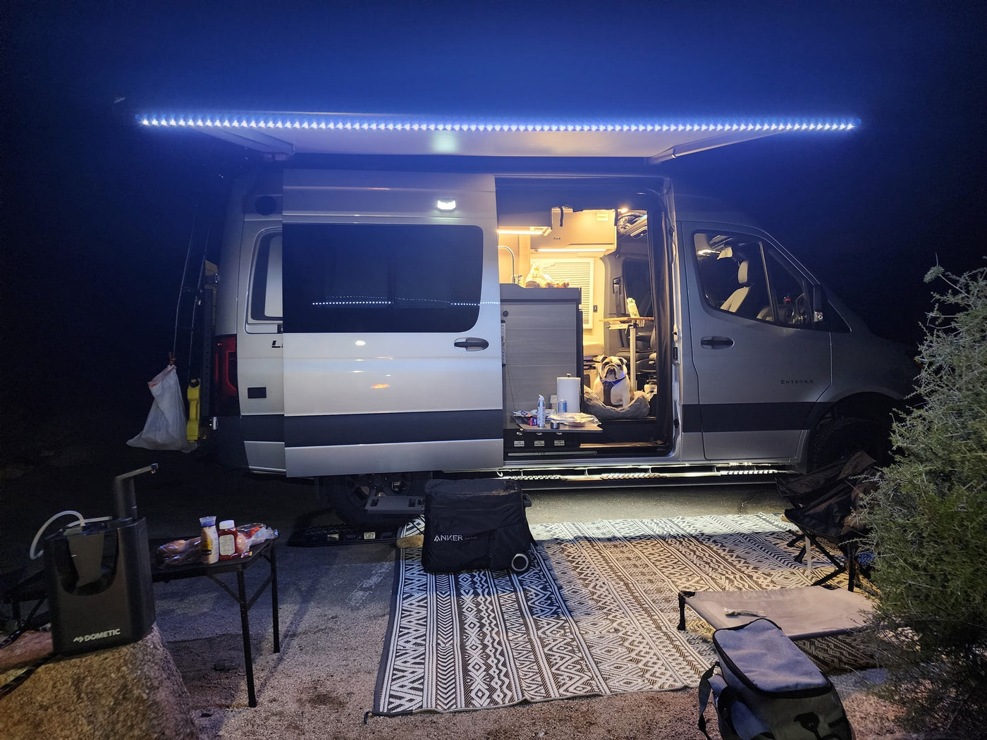 Cozy night in an RV rental with bright awning lights, an outdoor rug, and a happy bulldog enjoying van life. — photo 7