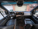 RV rental interior view: Dashboard, steering wheel, and front seats, with a house visible through the windshield.