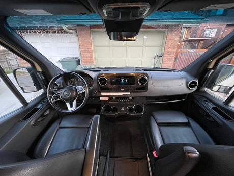 RV rental interior view: Dashboard, steering wheel, and front seats, with a house visible through the windshield.
