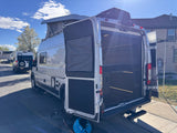 White camper van RV rental with open rear doors, pop-top roof, and AC unit. A second similar van is parked behind it.