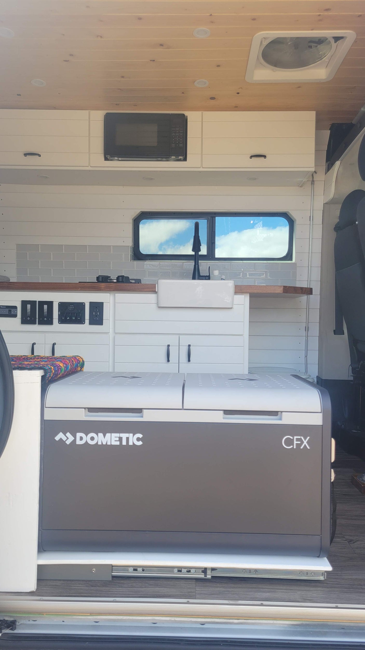 Modern rv rental camper van kitchen with sink, microwave, and pull-out Dometic CFX cooler.