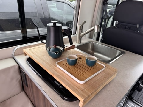 RV rental kitchen setup with a gooseneck kettle, teapot, and tea cups on a bamboo tray next to a compact sink.