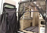 RV rental camper van interior showing a foldable bed, storage, rear bug net, and outdoor privacy screen.