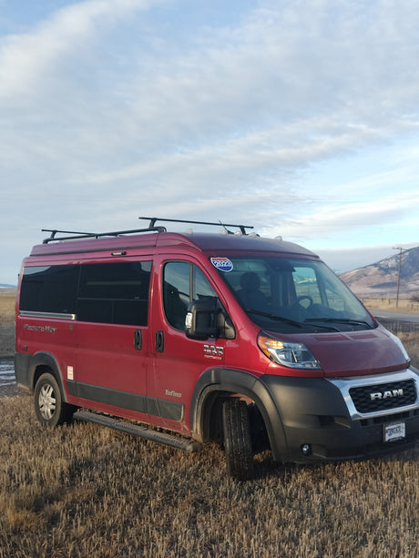 Explore landscapes with this red Pleasure-Way Tofino camper van, an ideal rv rental, parked in a dry field with mountains.