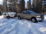 Truck & NO-BO RV trailer in snow, a dog peeks out. Explore winter with an rv rental.