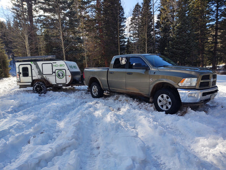Truck & NO-BO RV trailer in snow, a dog peeks out. Explore winter with an rv rental.