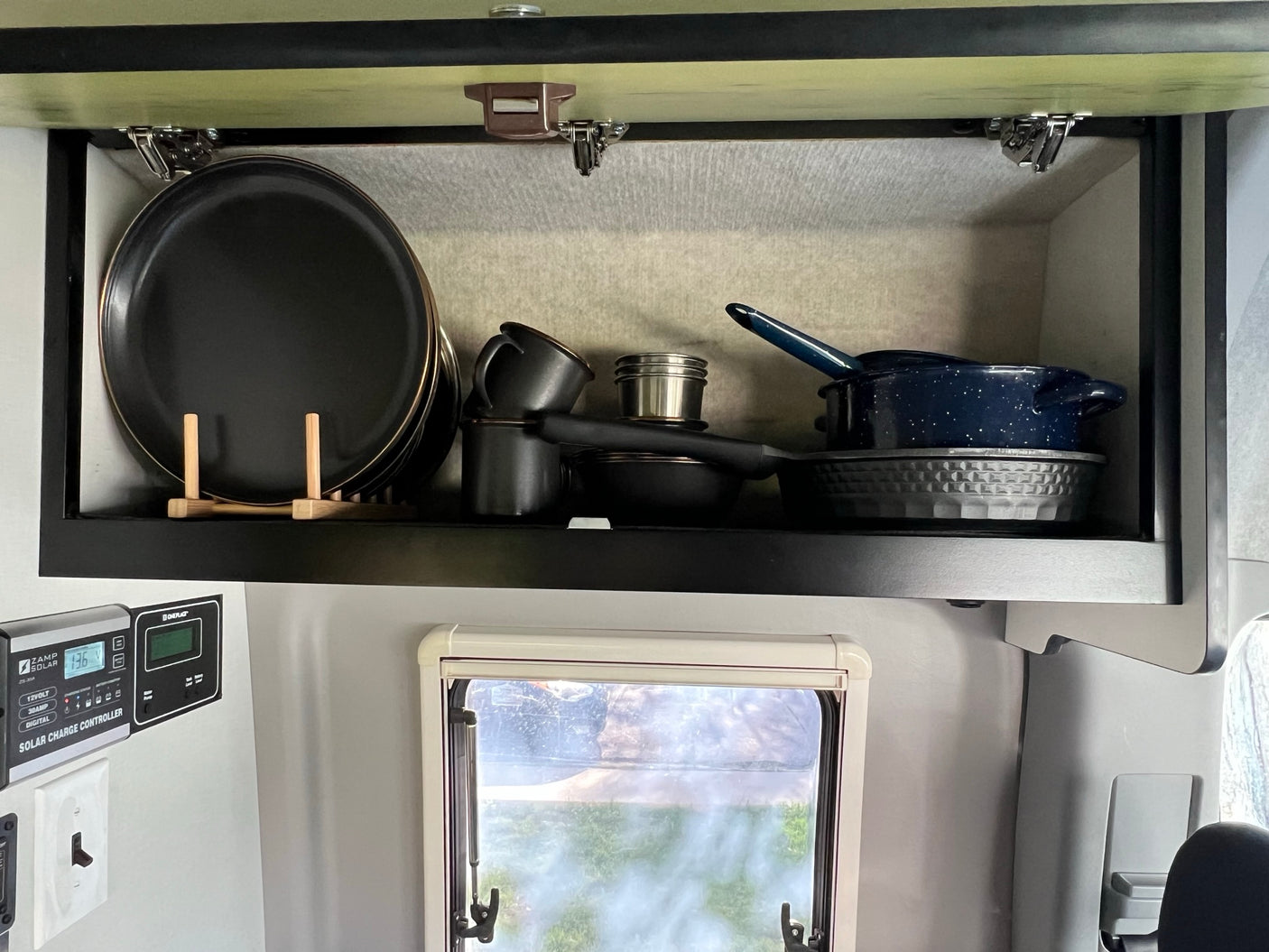 RV rental: An organized kitchen cabinet with black plates, pots, and pans, plus a Zamp Solar charge controller display.