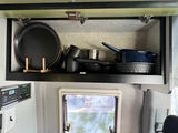 RV rental: An organized kitchen cabinet with black plates, pots, and pans, plus a Zamp Solar charge controller display.