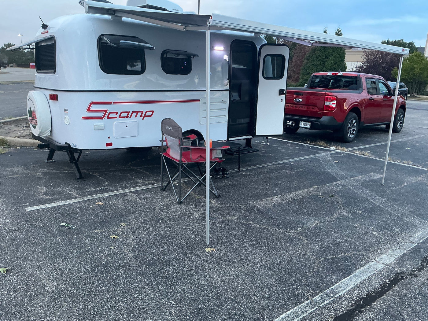 Scamp travel trailer RV rental with extended awning, parked in a lot next to a red Ford Maverick pickup truck.
