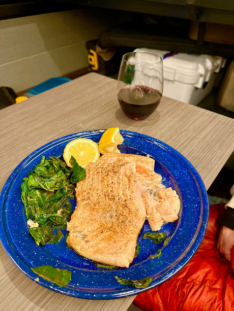 Cozy RV rental dinner: perfectly cooked salmon with spinach and lemon, paired with red wine. Simple, tasty travel meal!