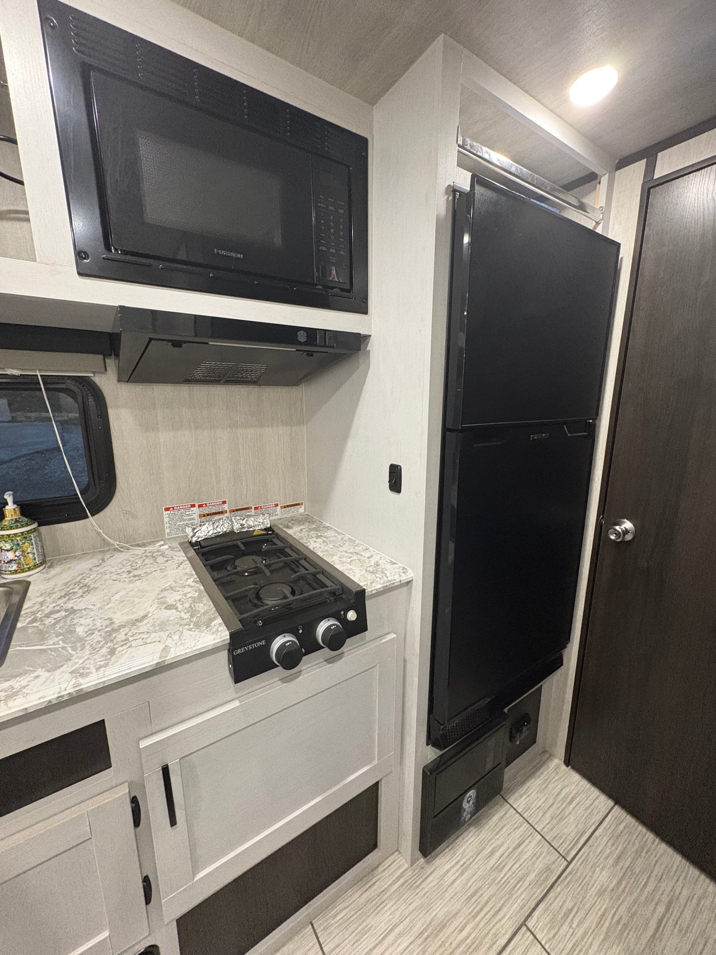 Compact RV rental kitchen with microwave, gas cooktop, and black refrigerator. Efficient, modern design.