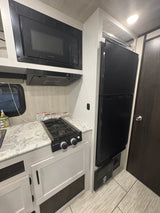 Compact RV rental kitchen with microwave, gas cooktop, and black refrigerator. Efficient, modern design.