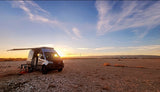An RV rental camper van parked in a wide-open desert, illuminated by the warm glow of a beautiful sunset. Perfect for outdoor adventures.