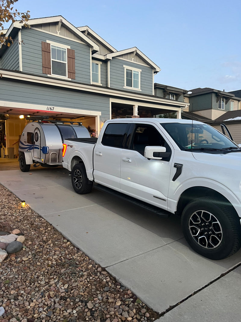 White Ford F-150 truck with silver teardrop RV rental hitched, partially in a garage with a person, ready for a trip. — photo 5