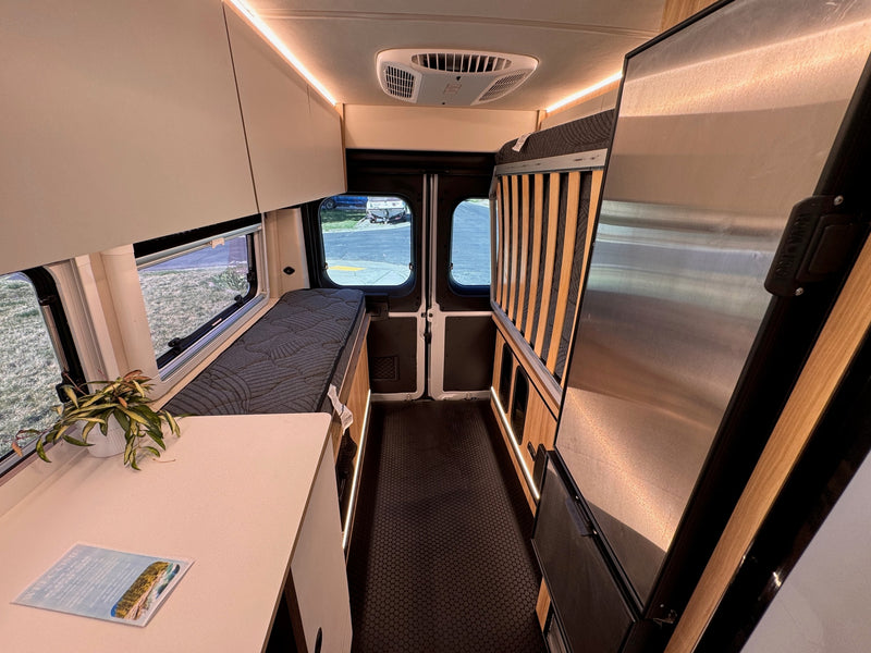 Bright rv rental camper van interior: compact kitchen, comfortable bench bed, refrigerator, and overhead storage with warm lighting. — photo 17