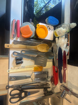 A collection of RV rental kitchen tools and cleaning supplies, including spatulas, knives, sponges, and wooden utensils, near a sink.