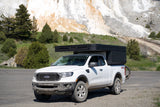 White Ford Ranger pickup with black overland camper, parked by nature's travertine terraces. An ideal RV rental for adventure.